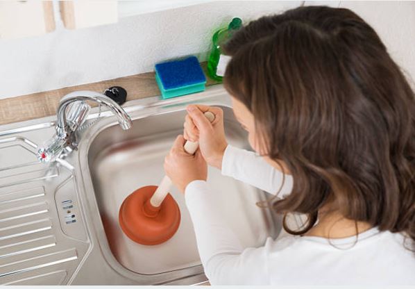 A plumber inspecting a damaged pipe under a sink in a residential property.